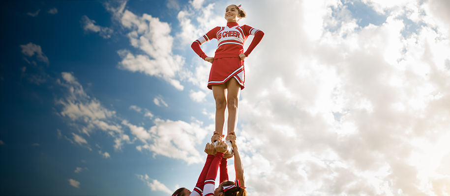 Cheerleader in red and white uniform backed by clouds, held up by teammates