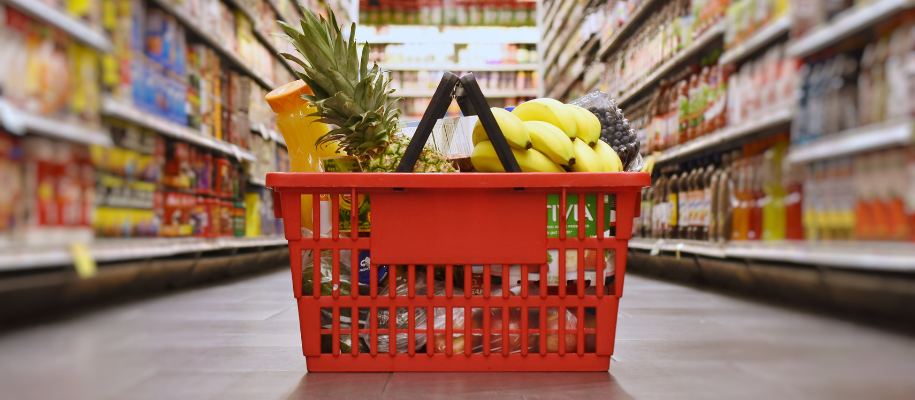 Red grocery basket filled with orange juice and fruits on floor of store aisle