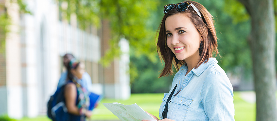 White female students holding paper outside on campus, smiling