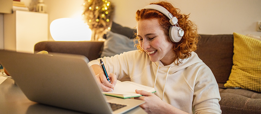 Young White person, curly red hair, learning in living room, writing in notebook