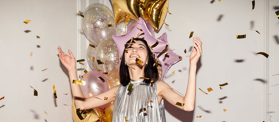 Asian woman in sparkling silver dress looking up with confetti and balloons