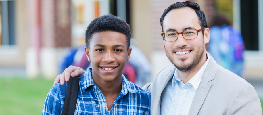 Black male student smiling with Asian male teacher outside 