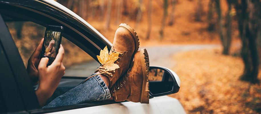 White person taking picture of boots and leaf sticking out of car window in fall