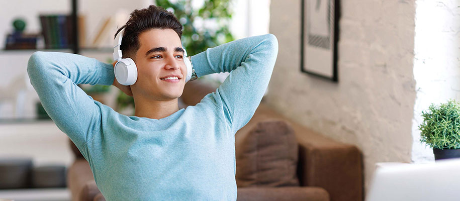 Relaxed Latino student wearing headphones, with arms behind head, smiling