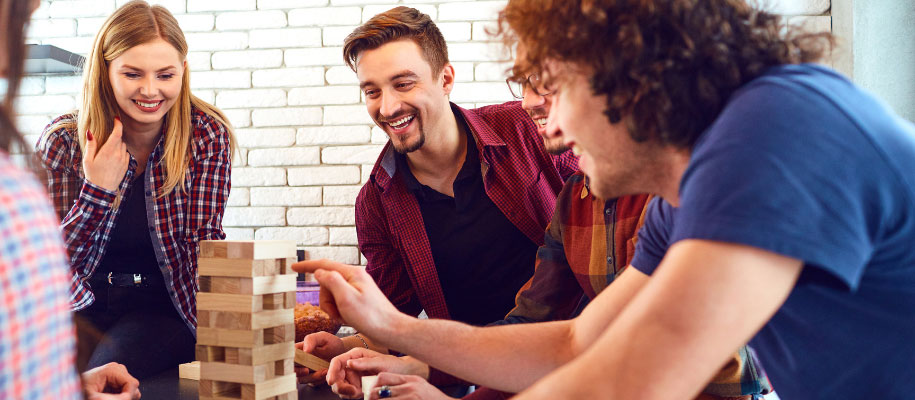 Group of students in dorm gathered around table playing Jenga and laughing