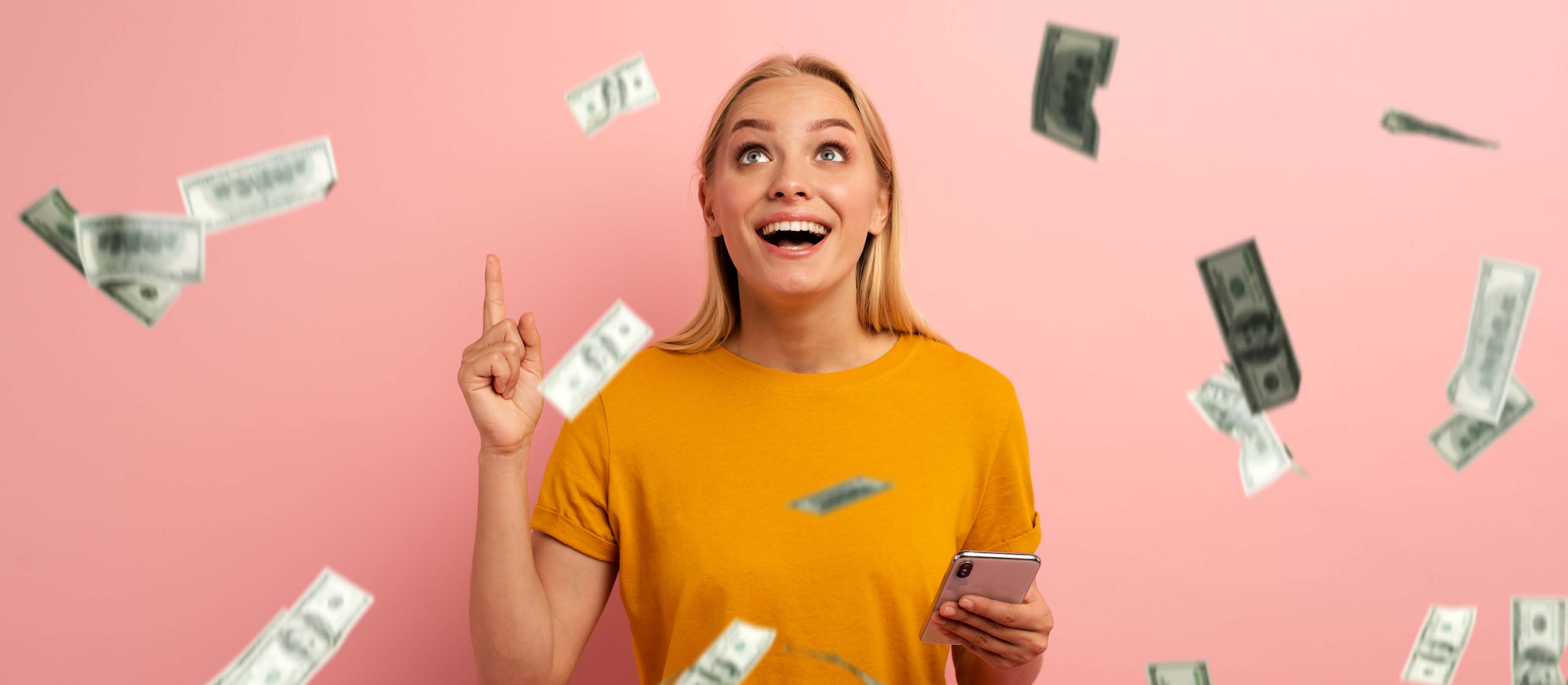 Excited White blonde holding phone and pointing at ceiling with money falling