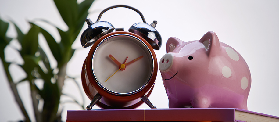 Polka-dotted pink piggy bank sitting on book next to alarm clock with no numbers