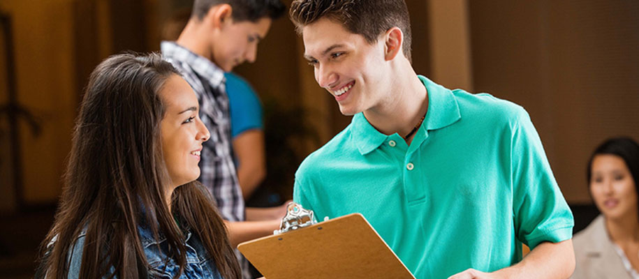 White male student holding clipboard recruiting White female at activities fair