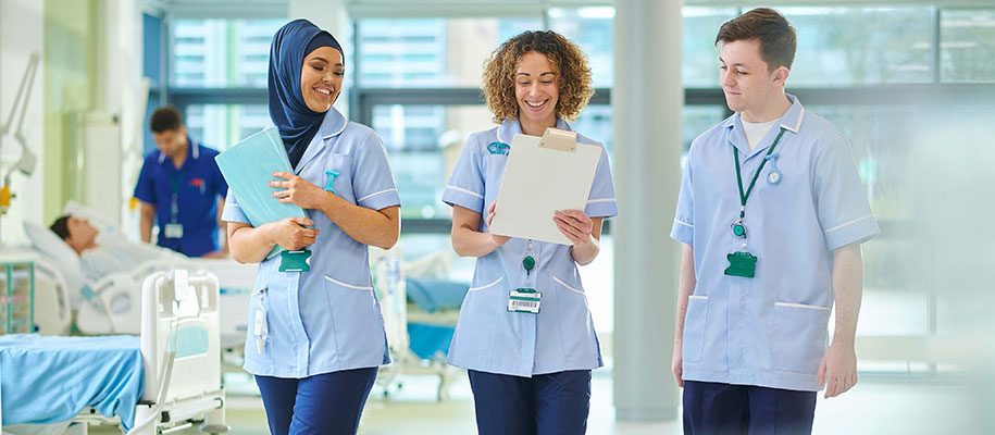 Woman in hijab, Black woman & White male in nursing scrubs walking in hospital
