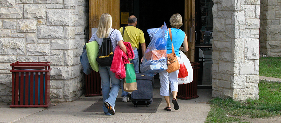 White family of three walking into building carrying daughter's move-in stuff