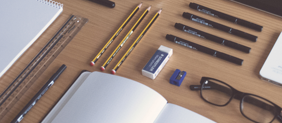 Wood desk with pencils, eraser, pens, glasses, notebooks and more neatly aligned