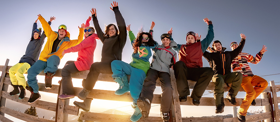 Group of college age people in winter ski gear sitting on wood fence