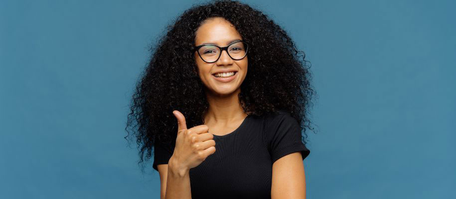 Black female student with curly hair and glasses, smiling and giving thumbs up