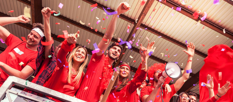 Group of young adults dressed in red at sporting event cheering with confetti