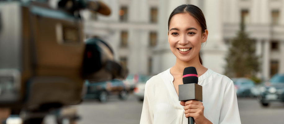Young Asian female broadcaster holding a microphone in front of a camera