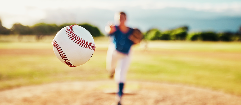 Focus on baseball thrown toward camera by woman pitcher in blurred background