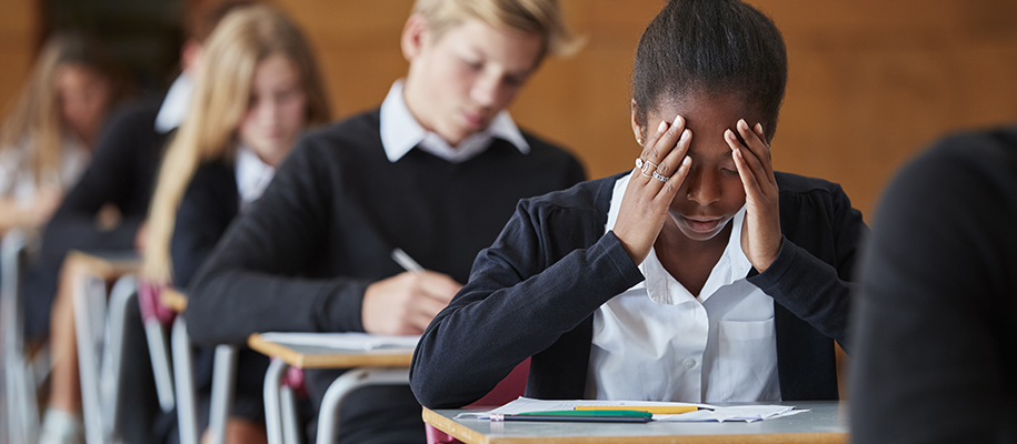 Black girl in school uniform with face in hands in row of desks taking a test