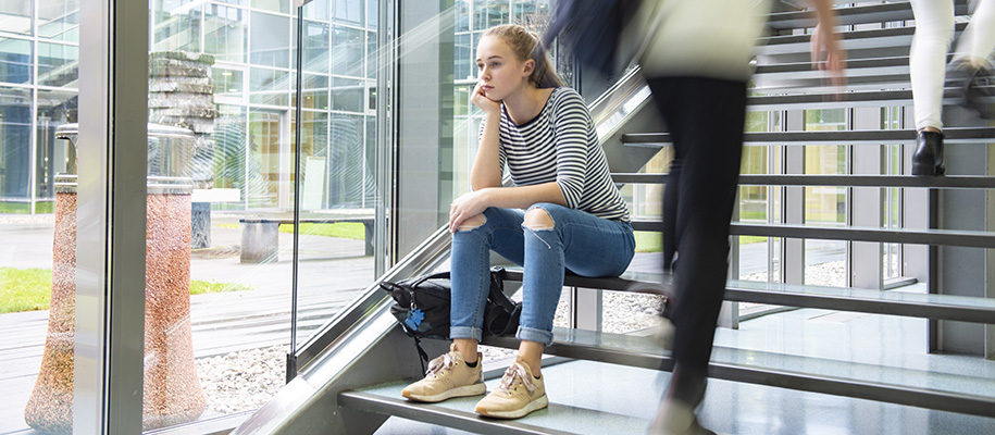 Blurred people walk by sad White woman sitting on steps of glass campus building