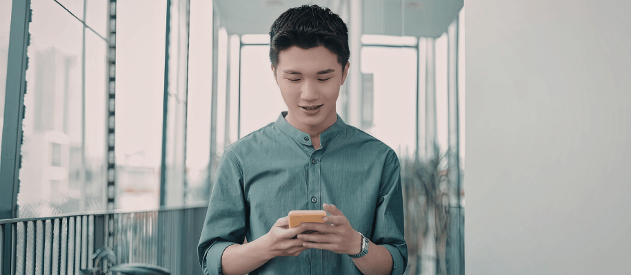 Young man walking while looking down at the cellphone held in both of his hands