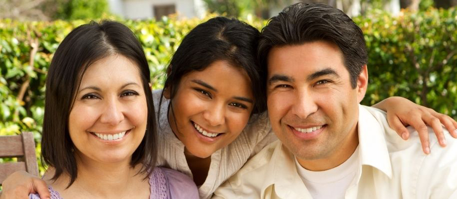 Hispanic family outside with daughter in middle of parents with arms around them
