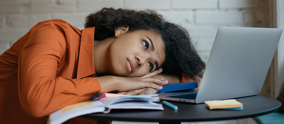 Black woman in collared shirt lying head on study stuff, looking sadly at laptop
