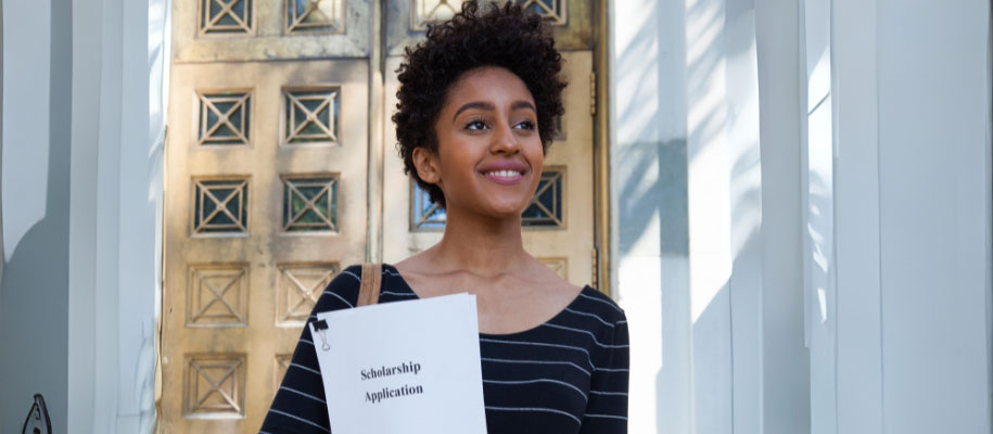 Black female with short curly hair smiling, holding scholarship application