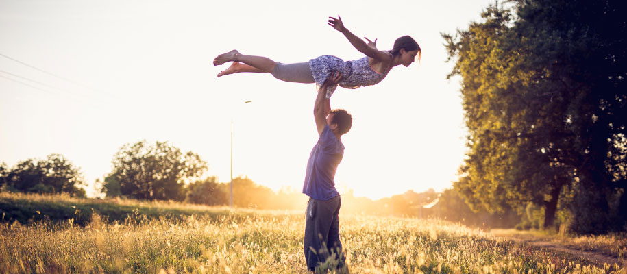 Young man lifting young woman in a field at sunset, Dirty Dancing style
