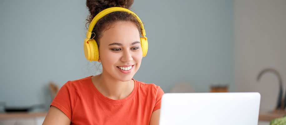 Young Black female student wearing yellow headphones, smiling at laptop