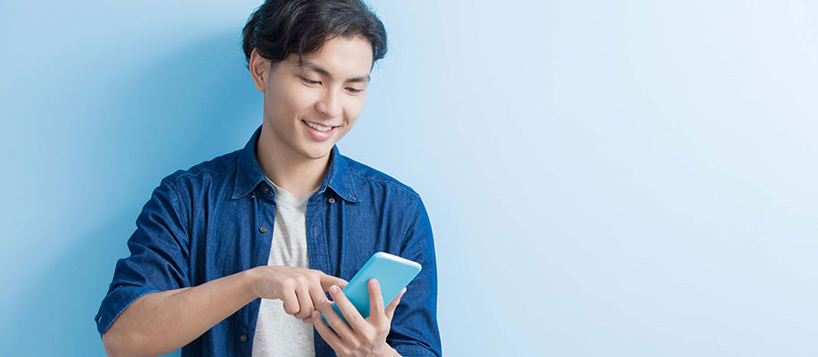 Asian male student in blue button-up smiling and pointing at smartphone