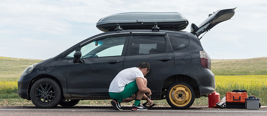 White man in workout shorts and t-shirt crouching next to car after putting on spare tire