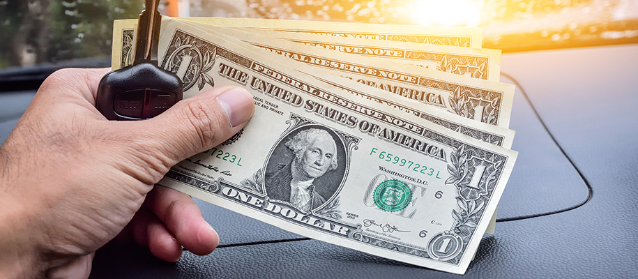 Hand of White person holding car key and five dollar bills in car