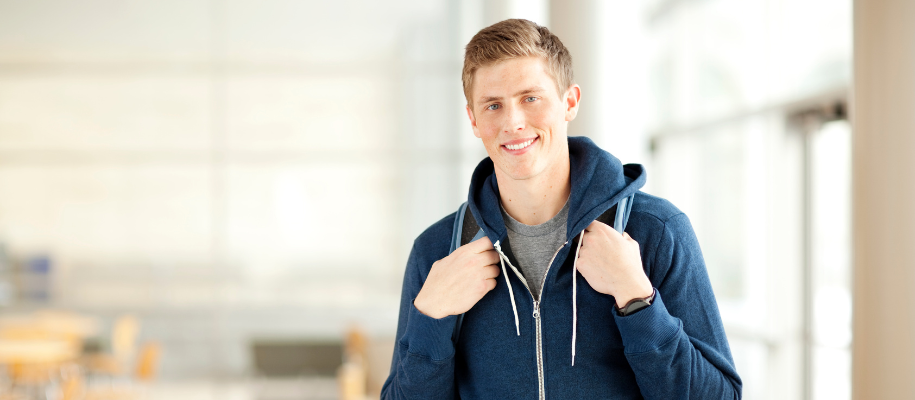 White male student in dark blood hoodie in empty classroom, smiling at camera