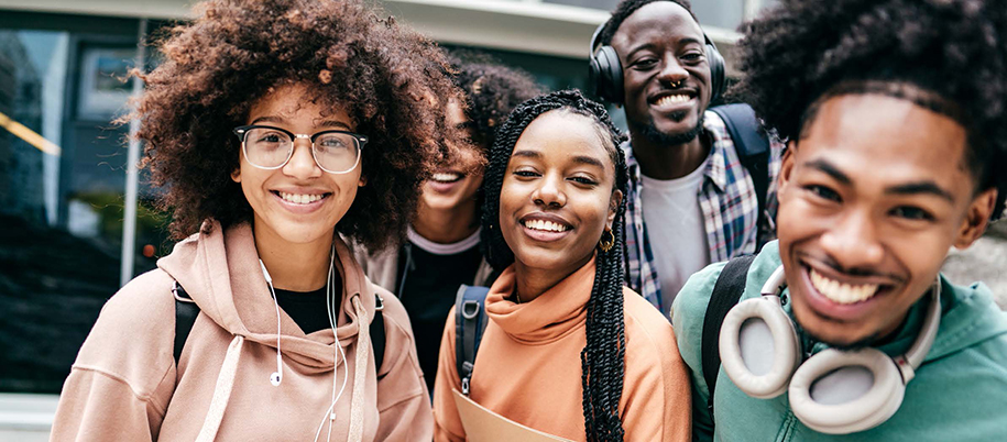 Five Black students of varying skin tones smiling with headphones and backpacks