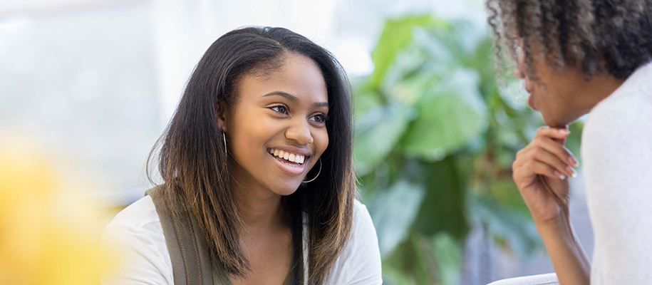 Black female student smiling at Black counselor with hand on chin with plants