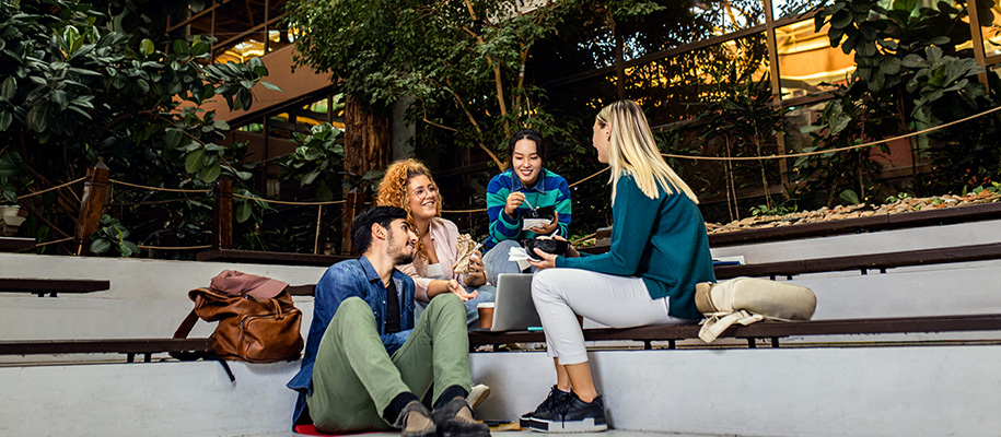 Four diverse community college students eating lunch in atrium on campus