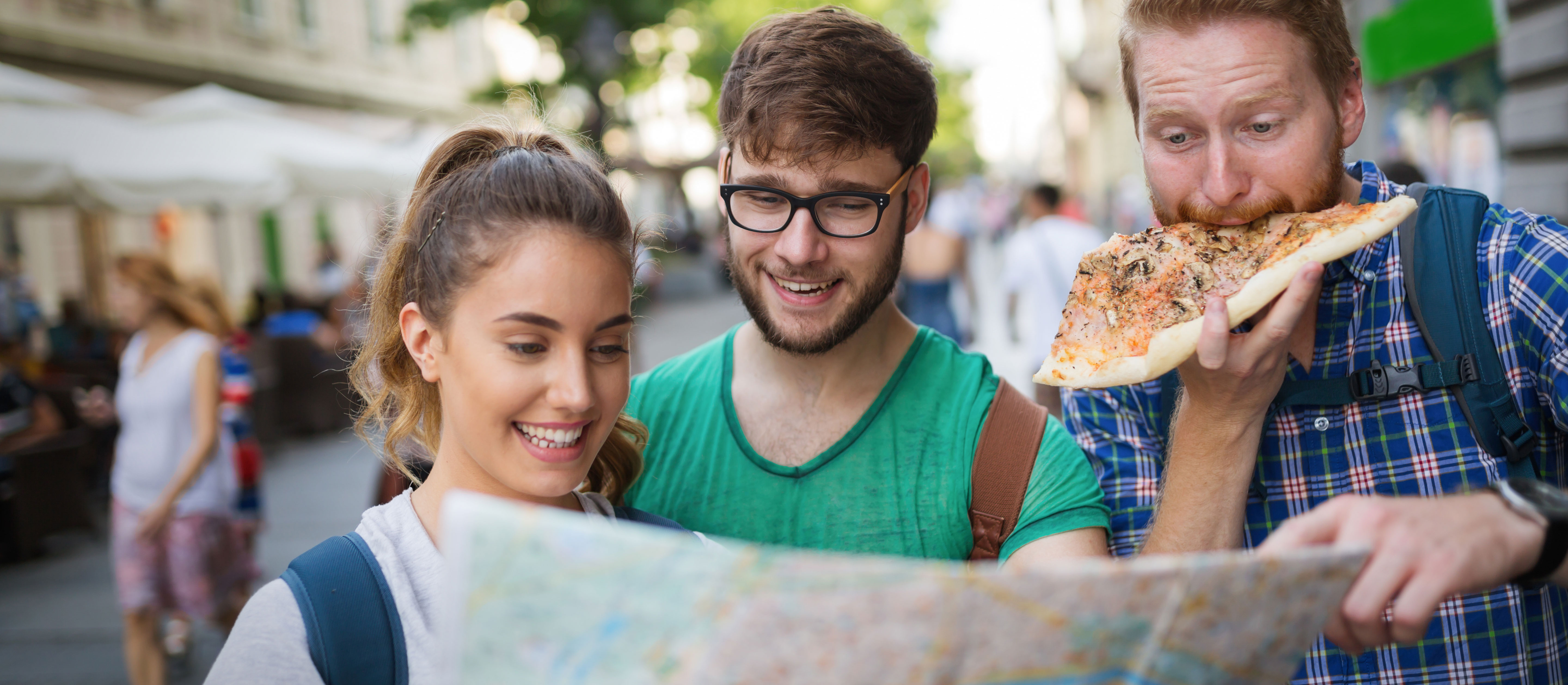Happy group of tourists traveling with map, sightseeing in city, eating pizza