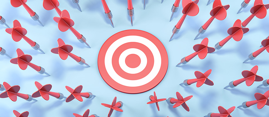 Target on blue backdrop surrounded by red darts that have missed it