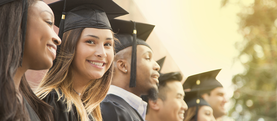 Brunette woman in grad cap and gown smiling at camera in line of other graduates
