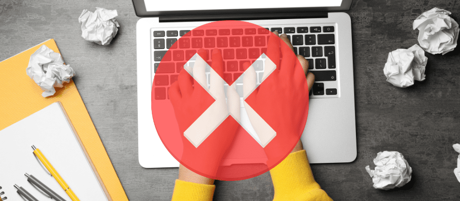 Hands in yellow sweater typing on keyboard, surrounded by crumpled paper, red X
