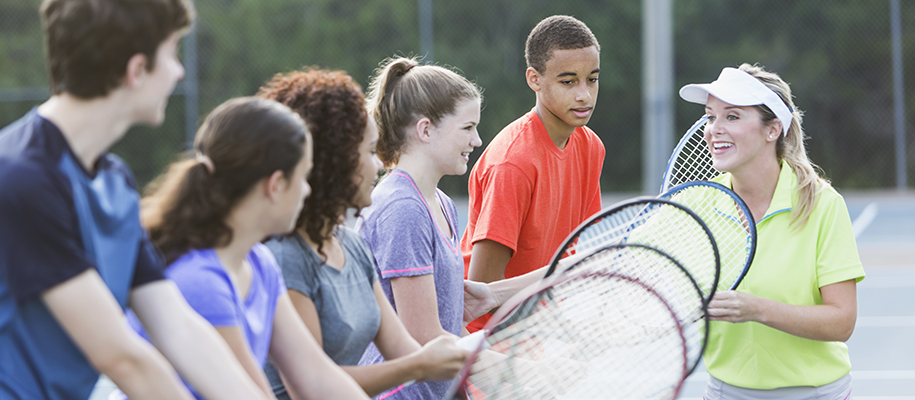 Diverse group of student learning to play tennis from White blond female coach
