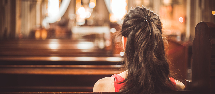 Back of White woman with brown hair and red shirt sitting in church pew