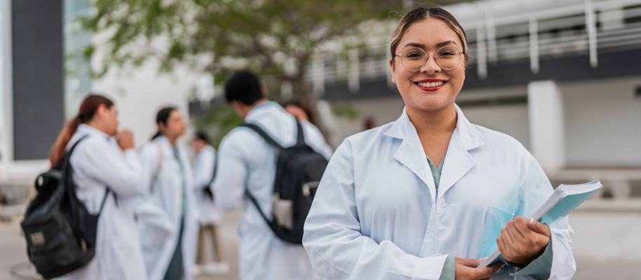 Latina woman in glasses, red lipstick, medical coat, holding book outside