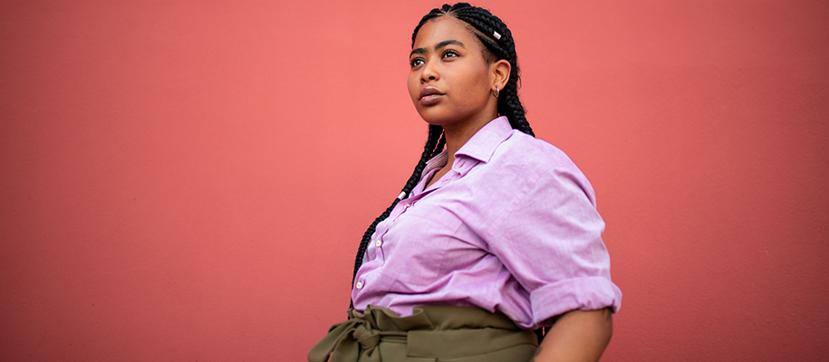 Plus-sized Black woman in purple shirt with long braids against red backdrop