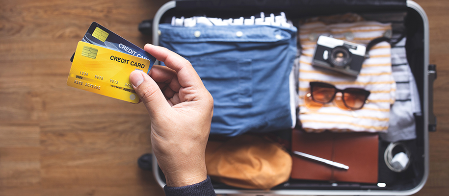 Hand of White person holding two credit cards over packed suitcase for a trip