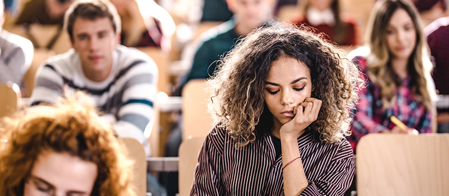 Black student with curly hair in striped shirt in lecture classroom bored