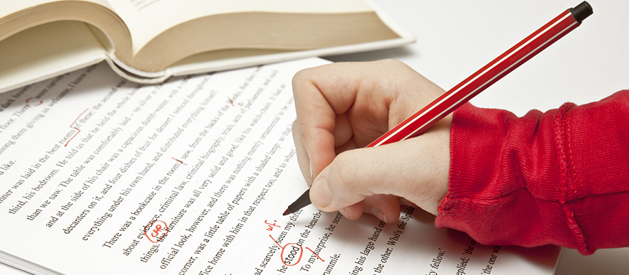 White hand in red sleeve holding red pen over essay with edit marks