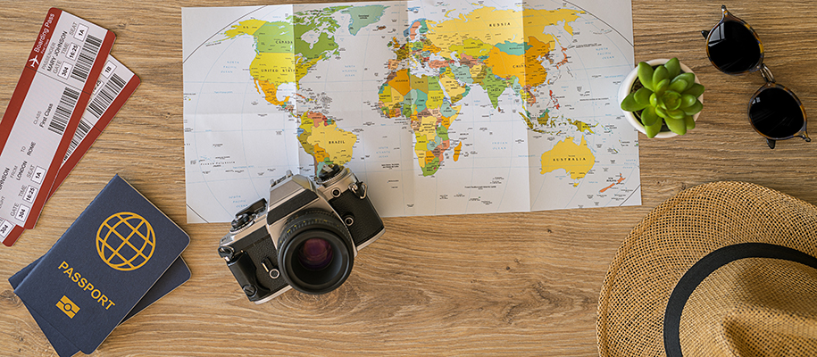 World map, plane tickets, passport, hat, camera, plant, sunglasses on table