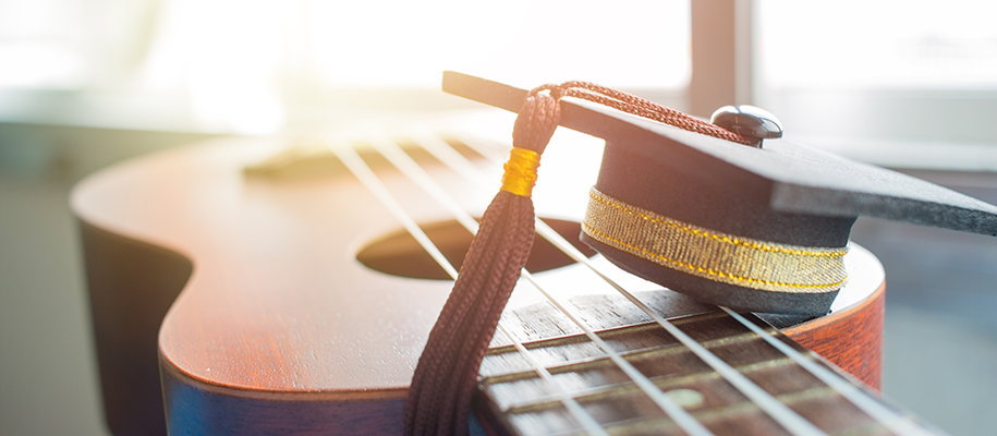 Closeup on ukulele in the sun with tiny graduation cap on top
