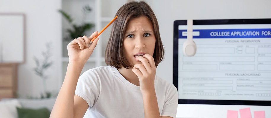 White teen girl with pencil to head, fingers to mouth, stressed over college app