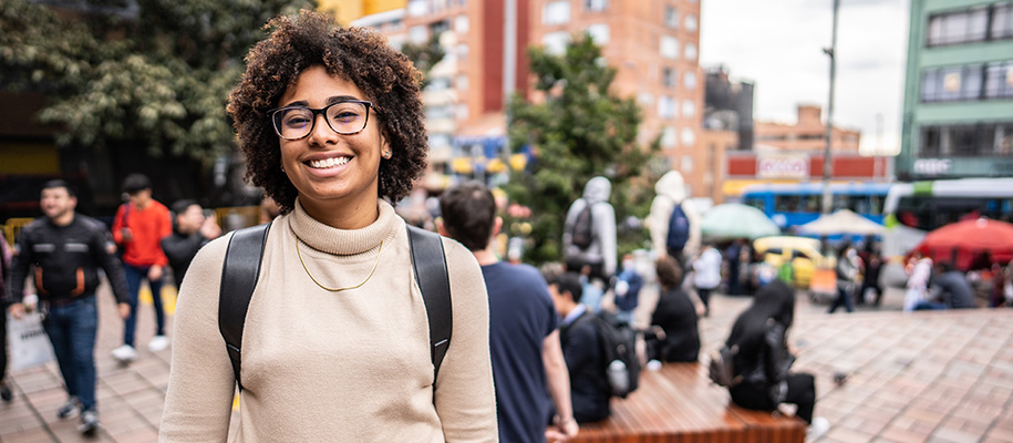 Young Black woman with afro and glasses smiling in busy outside city center